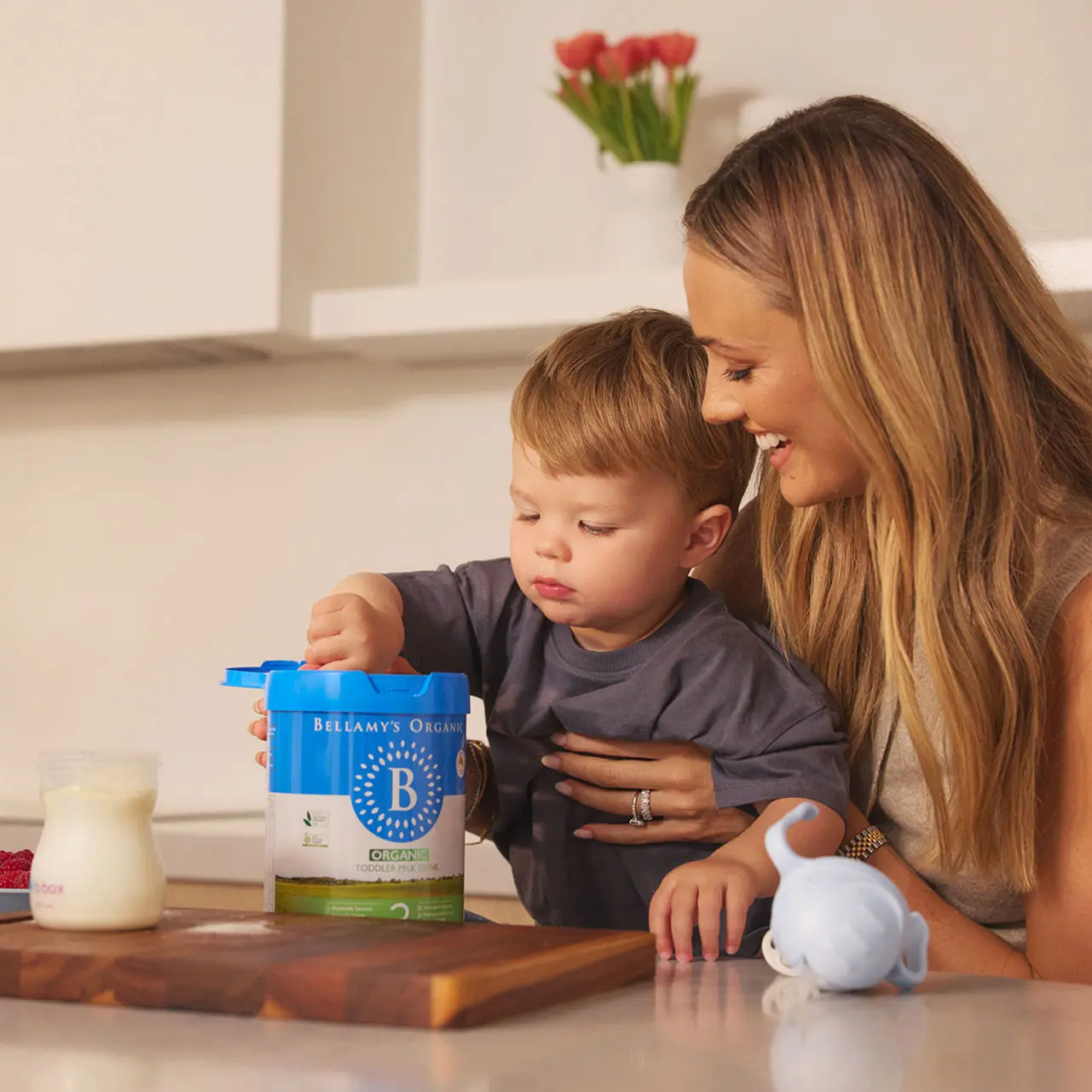 Mum helping toddler scoop Bellamy’s Organic baby formula in kitchen – discover more at Baby Expo Sydney, Koala Korner zone.